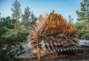 Iso puinen veistos, jossa lehtimäisiä ulokkeita, ympärillä metsää