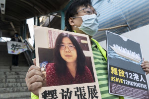 Journalisten Zhang Zhan fängslades i maj för att ha spridit problem i samband med att hon rapporterade om coronautbrottet i Wuhan, Kina, i februari. Inför hennes rättegång demonstrerade flera personer utanför domstolsbyggnaden. En man håller upp ett plakat med bild på en svarthårig kvinna och kinesiska tecken.