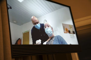 När Jytte Margrete Frederiksen vaccinerades i Danmark följde statsminister Mette Frederiksen med via videolänk. Bild på en skärm där en kvinna vaccineras.