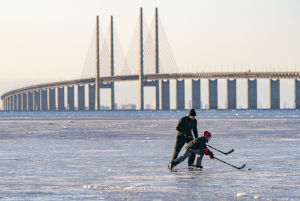 Malmö- och Köpenhamnsborna är vana vid att bara ta bil eller tåg över bron för att nå jobb, vänner och familj i grannlandet. Man och barn spelar hockey på havsisen, med Öresundsbron i bakgrunden.