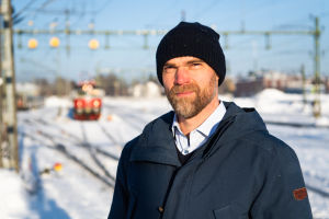 Stefan Linder ansvarar för nattågstrafiken mellan Luleå och Stockholm. Man står framför tågdepå med tåg och spår i bakgrunden.