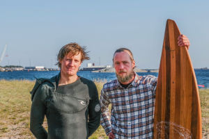 Mikael Hyryläinen ja Joachim Lindholm seisovat vierekkäin Tulliniemen rannalla. Joachimin vieressä puusta on tehty lainelauta.