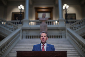 Georgias guvernör Brian Kemp undertecknade den omdebatterade lagen förra veckan. Brian Kemp står i en talarstol framför en ståtlig trappa.