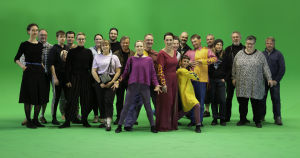 21 Mirages-elokuvan tekoon osallistunutta ihmistä seisoo ryhmässä vihreää kangastaustaa vasten.