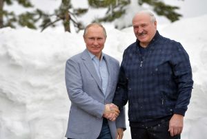 Putin och Lukasjenko skakar hand under sitt möte i Sotji i februari 2021. Rysslands president Vladimir Putin och Belarus president Aleksandr Lukasjenko skakar hand och tittar båda mot kameran.