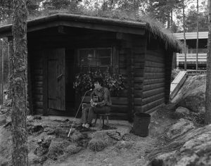 Donovan Paimion motellin savusaunalla. Valmiissa ohjelmassa moderni majoituslaitos ei häirinnyt luonnonläheistä tunnelmaa. Folklaulaja Donovan Ohimennen-ohjelman kuvauksissa Paimion motellin savusaunan edustalla. Motelli kuvassa taka-alalla.