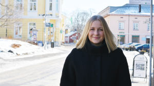 Anita Westerholm är invald i kommunfullmäktige och är stadsstyrelsens andra vice ordförande. En bild på en kvinna i svart vinterjacka som står vid ett torg. I bakgrunden syns färgglada hus.
