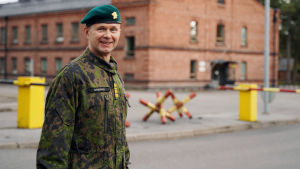 Mika Immonen är nöjd med lösningen. Stabchef Mika Immonen står vid porten till ett garnisonsområde. Han ler och tittar in i kameran.