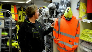 Camilla Bärlund vill i fortsättningen fokusera på den egna verksamheten. En kvinna i står i en butik omringad av gula och orangea arbetskläder.