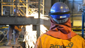 Gnistorna flyger när engelsmännen går loss på gammalt järnskrot i fabrikshallen. En man med orange halare och vit skyddhjälm ser på när en annan person bränner sönder metallskrot i en fabrikshall.