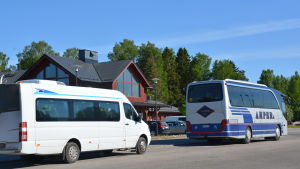 En större taxi och en buss står parkerade vid en affärsfastighet i rött trä.