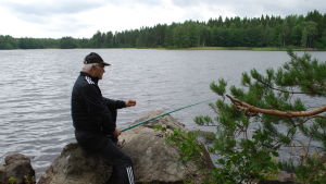 79-åriga Arvo från Humppila brukar komma hit med sina vänner ett par gånger i månaden. En äldre man metar vid en sjö.