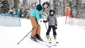 Carolina och Sebastian Sved trivs i slalombacken. En kvinna och ett barn på slalomskidor i slalombacke. De ser in i kameran och ler.