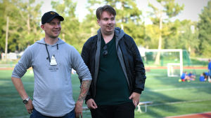 Toni Wistbacka (t.v.) och Dan Sandberg har stenkoll på finländsk fotboll. Toni Wistbacka (t.v.) och Dan Sandberg står vid en fotbollsplan.