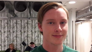 Sveriges försvar är svagt och behöver all hjälp det kan få, säger Daniel Fred. Daniel, i närbild, grön tröja, tapeter med björkar i bakgrunden, skolans aula.