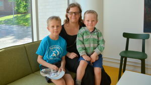 Till vänster Lukas Hellman, Pia Hellman och Kasper Hellman En mamma sitter med sina två söner på en soffa framför ett fönster