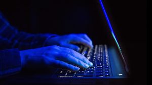 Problemet på nätet är inte ungas dåliga beteende, utan de vuxnas. Närbild på en laptop. På tangentbordet är två händer som lyses blåa av skenet från skärmen.