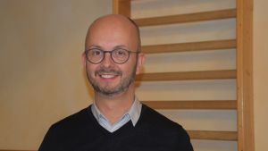 Mathias Nyström har fixat bland annat programblad till skoloperan. Plus cirka tusen andra saker som sköts bakom kulisserna. En glasögonprydd man står i en jumppasal (skola) och ser in i kameran.