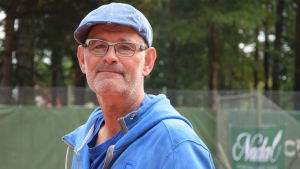 Johan Krause sitter i styrelsen för Hangö tennisklubb. Profilbild på en glasögonprydd man i blå keps och blå munkjacka på en tennisbana.