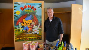 Kaj Itämäki är glad att kunna föra filmerna nära Sibboborna En man står bakom ett bord med biosnacks och brevid en plansch på bamse