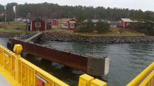 För öborna är diskussionen bekant, men de ger sig inte. En färja räcker inte, säger de. Utsikten mot röda trähus på stranden i Kittuis från landsvägsfärjan som anländer till Houtskär.