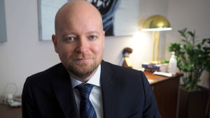 Frågar man undervisningsministern säger han att han verkligen hoppas att alla studerande ska kunna få närundervisning, men han kan inte säga när. Manlig minister i mörkblå kostym i sitt arbetsrum