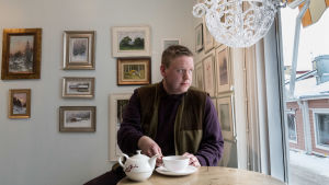Företagaren Leo Kallio anser att Borgå borde få mer ut av att agera filmkuliss. En man sitter med en vit tekopp framför sig, på bordet vit tekanna med röda blommor, mannen tittar ut genom fönstret. I bakgrunden gammaldags tavlor.
