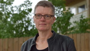 Kirsi Ala-Jaakkola leder arbetet inom äldreservicen. Kvinna ser in i kameran, allvarlig. Bakom ett staket och ett lövträd. Sommar