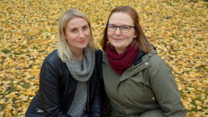 Sofie Björklund och Sara Tallsten har koll på motions- och kulturpasset. Sofie och Sara sitter på huk och tittar in i kameran och ler. Massa orange löv i bakgrunden.