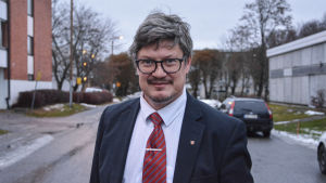 Rurik Ahlberg. Medelålders man i kostym står på väg, tittar in i kameran med ett litet leende.