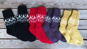 Näsdagssockor i alla näsdagens färger Fyra par handstickade yllesockor i färgerna svart, lila, rött och gult,med vitt hjärtmönster. Modellen är näsdagssockan 2020.