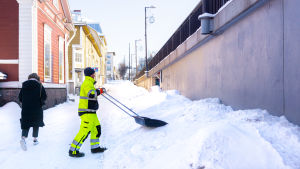 Tom Kristén från Borgå stad putsar gatorna dagen efter ett ordentligt snöväder i tisdags. "Trevligt att arbeta utomhus, men nog skulle det kunna bli vår nu", säger han. En man i neonfärgad arbetsdräkt skyfflar snö vid kanten av den slätplogade trottoaren, en person med ryggen åt kameran går längs trottoaren, vädret är soligt.