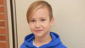 Milton Lehtinen går i tredje klass i Höjdens skola i Tenala. Han trivs i skolan. En tioårig pojke med blå munkjacka. Fotor taget inomhus mot en beige-grå vägg.