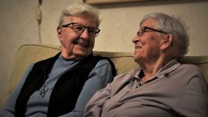 Birgit och Viola hör nu till de relativt få som finns kvar som genomlevt krigstiden och kan berätta om hur det var. Två äldre kvinnor ser mot varandra och ler.