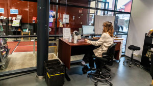 Helena Backman-Karvonen ger betjäning genom lucka. Bibliotekarie vid en disk.