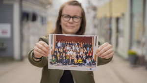 Skolfoto från Ekenäs gymnasium 2007. Ungefär hälften har inte flyttat tillbaka, än i alla fall. En kvinna håller fram och visar ett klassfoto.