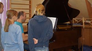 Kristoffer Holmberg säger att gitarren är hans instrument, men visst ser han ganska van ut vid flygeln också, eller hur? Barn runt ett piano/en flygel. En man sitter och spelar.