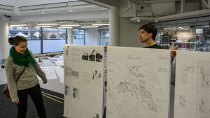 Generalplanläggare vid Vasa stad, Annika Birell, säger att det varit spännande att ta del av de studerandes kreativa idéer. En kvinna tittar på tre stora planscher med ritningar som en man står bakom och håller upp.