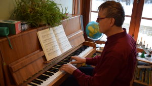 Michael Lettenmeier vid pianot, som upptar största delen av det lilla vardagsrummet. Även boendet är anpassat till klimatet, det är avsiktligt trångt. Man spelar piano i röd skjorta.
