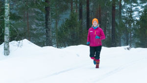 Maria Rosenström på morgonrunda - utan skor. En kvinna springer i skogen genom snön, hon har färggranna yllesockor på fötterna.