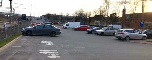 Parkeringarna på andra sidan banan finns bland annat vid affärerna. Den här bilden är från Lidls parkering 28.4, några dagar innan den avgiftsbelagda parkeringen togs i bruk på stationsområdet på andra sidan bangården. Personbilar som står parkerade på en affärs parkering. Till vänster syns järnväg. Andra affärer och hus i Karis centrum syns i bakgrunden. Den nya järnvägsbron syns också i bakgrunden. Kväll, solnedgång. Vår.