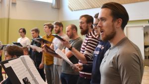 Rasmus Kurtén och resten av Akademen tränar intensivt inför nästa konsert - Jubileumskonserten i april. Akademen övar och sjunger med noter i hand i en gymnastiksal.