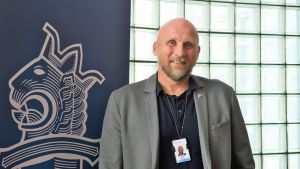 Polisinspektör Måns Enqvist jobbar med att förbättra samarbetet med finska romer. En kavajklädd man står intill polisens blåa banderoll med polisens vapen på.