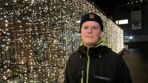 Atte Österholm känner julgubben väl. Atte Österholm utomhus vid vägg med julbelysning.