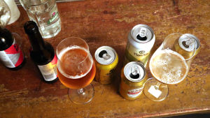I centrala Helsingfors tog lådvinerna slut på många Alko när människor bunkrade upp. Lådvinerna föredras av alkoholister, säger Christer Schoultz. Ölglas och ölburkar på ett brunt bord.
