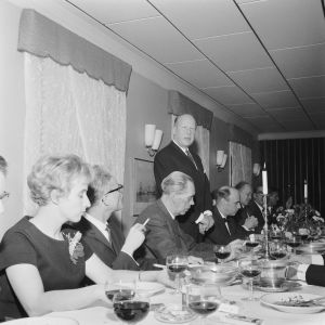 Festmiddagen med anledning av invigningen av den nya studion i Ekenäs 1964. Mannen som håller tal är Ekenäs stads representant Sven Högström. I förgrunden Maj-Britt Paro från Yle och Västra Nylands chefredaktör Frank Jernström. Till höger om Sven Högström syns även Christoffer Schildt, chef för svenska verksamheten på Yle. Ett antal personer vid ett middagsbord. En man håller tal. Mannen heter Sven Högström.