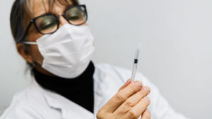 För att stoppa muterade coronavirus från att sprida sig i Finland krävs att man sätter fart på vaccineringarna och kväver epidemin, anser expertgruppen. Kvinna i glasögon o munskydd synar en vaccinationsspruta.