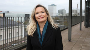Mirjam Kalland påminner om att även om familjen är det viktigaste för ett litet barn så njuter barnet också av att vara del av en större flock – en gemenskap som det fötts in i. Professor i småbarnspedagogik Mirjam Kalland ler mot kameran. Hon står utomhus på en bro.