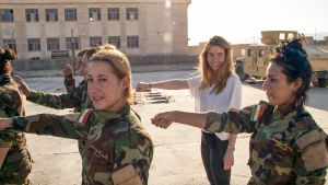 Stacey Dooley: Tytöt vastaan Isis. Naissotilaita ja toimittaja heidän kanssaan parijonosso, toinen käsi eteen ojennettuna.