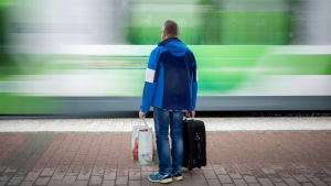 Många drar nytta av en snabb tågförbindelse mellan Åbo och Helsingfors, men kommer Västnyland att bli helt förbiåkt? En man väntar på ett tåg på perrongen, samtidigt som ett annat tåg susar förbi.